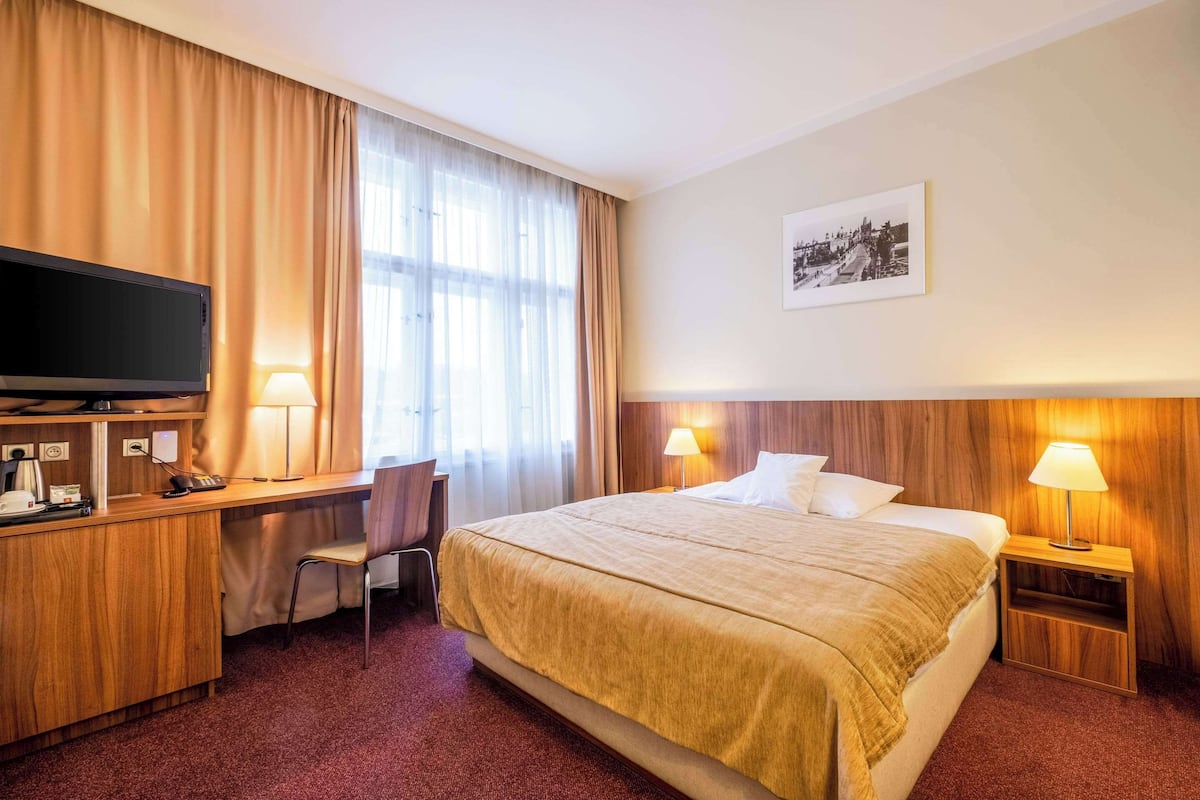 Een hotelkamer met een bed, bureau, stoel, televisie en lampen.