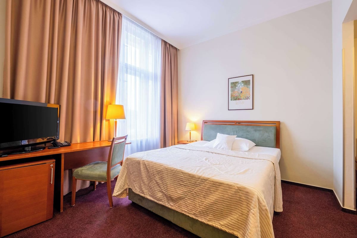 Een hotelkamer met een bed, een bureau met televisie, een stoel en een lamp.