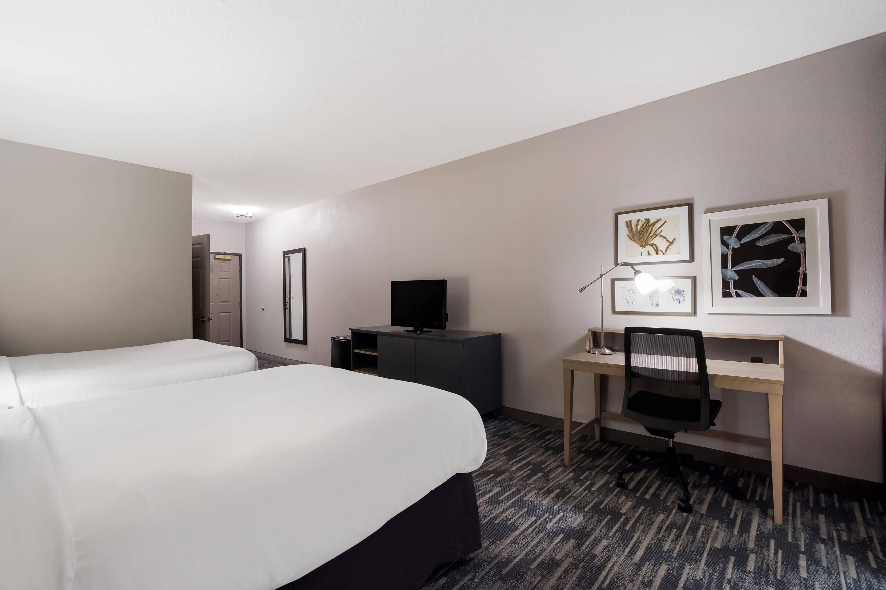 Una habitación de hotel con una cama, un escritorio, un televisor y cuadros en la pared.