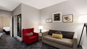 A hotel room with a red armchair, a beige sofa, a small table with a lamp, and a bed with a white headboard. - Country Inn & Suites by Radisson, Augusta at I-20, GA (Augusta)