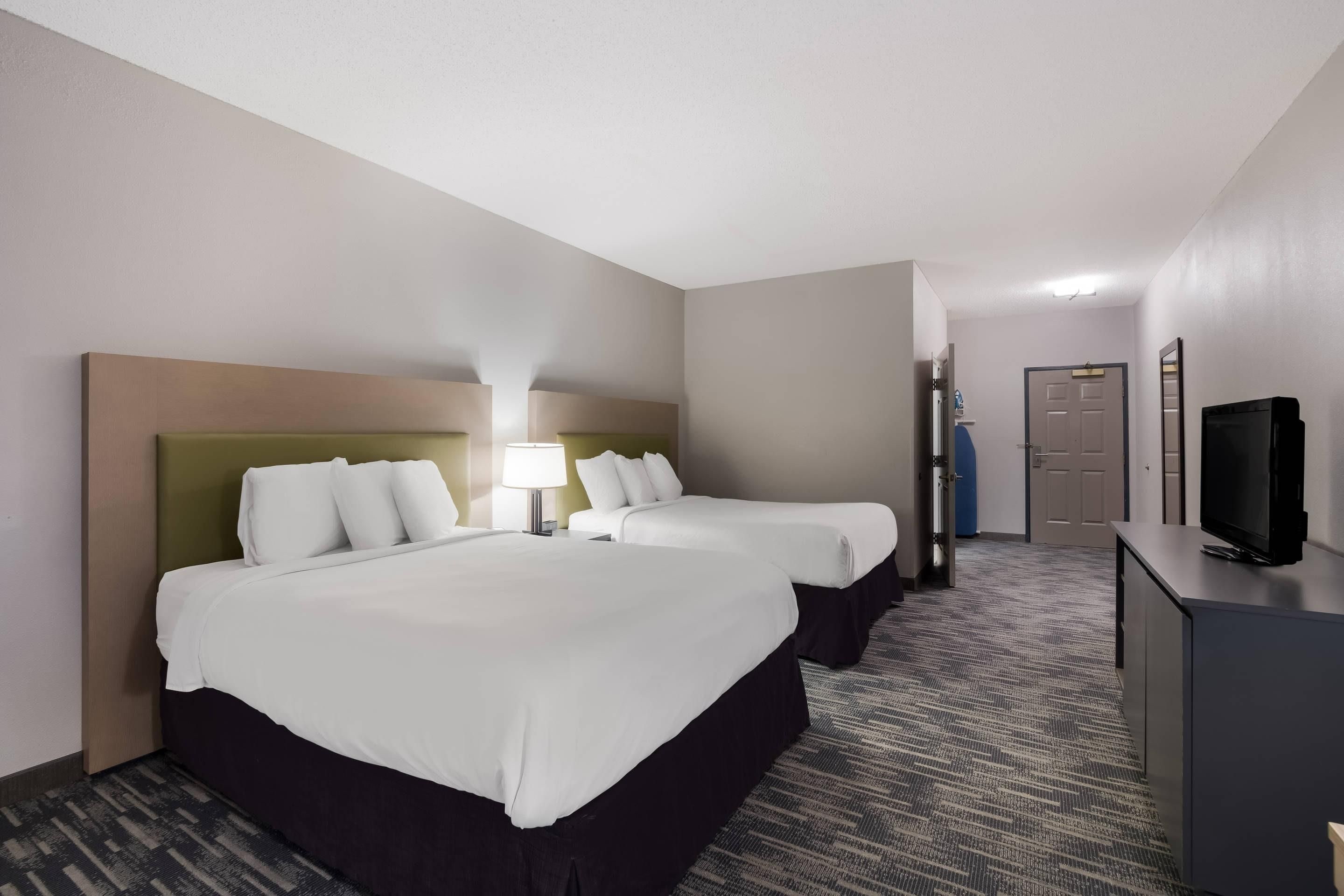 A hotel room with two beds, a desk with a television, and a door leading to a bathroom.