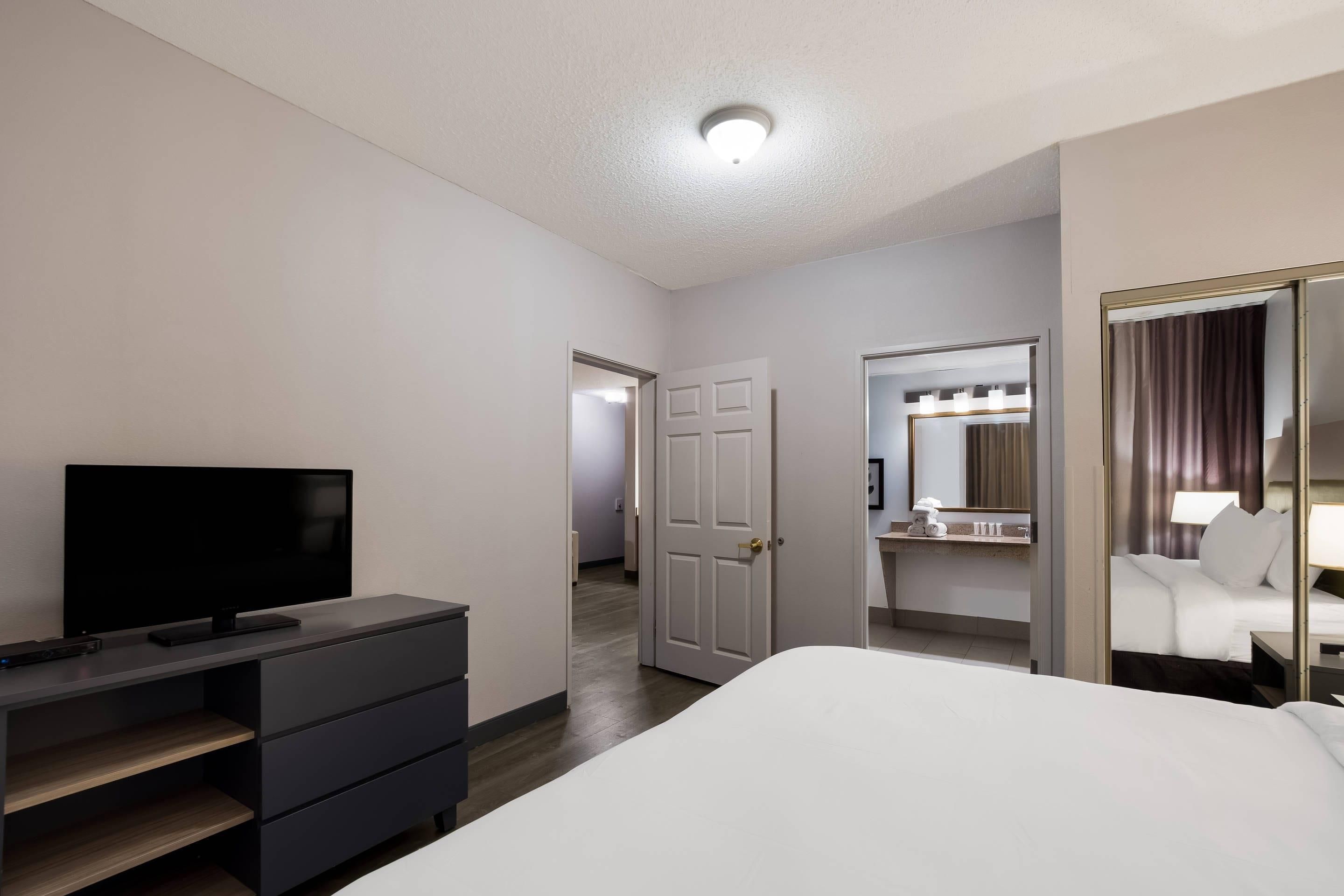 A hotel room with a bed, a TV, a dresser, a mirror, and a door leading to another room.