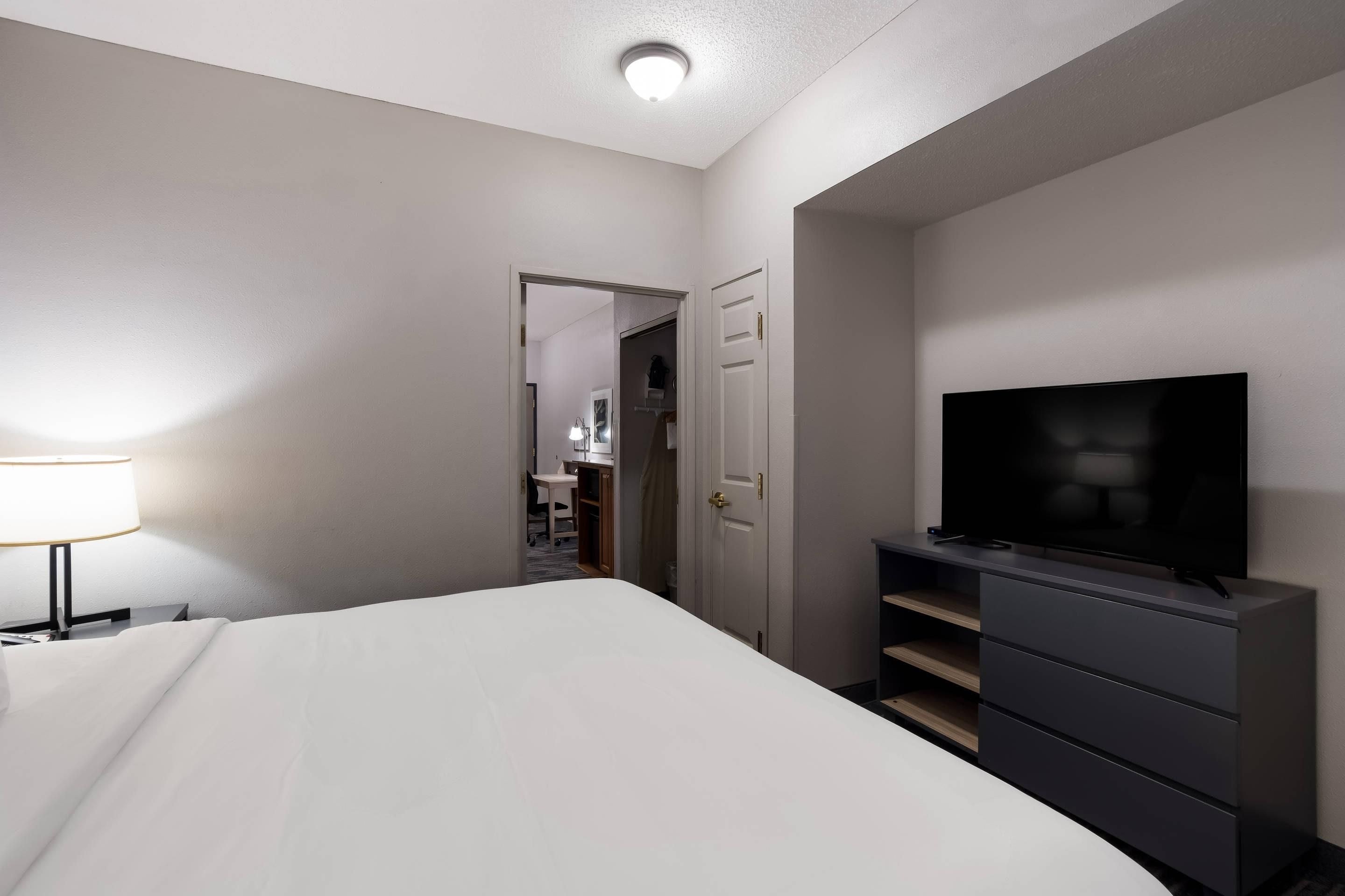 A hotel room with a bed, a television, a desk with a lamp, and a wardrobe.