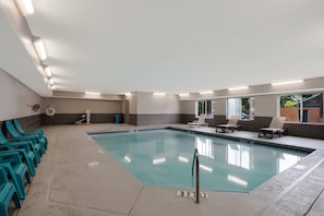 An indoor swimming pool with clear water, surrounded by lounge chairs and a changing room.