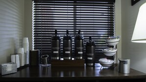 A bar area with four Highridge branded water bottles labeled 'Gourmet,' 'Decaf,' 'Bold,' and 'Hot Water.' There are stacked white cups, a metal basket, and a bowl on a stand. - Country Inn & Suites by Radisson, Augusta at I-20, GA (Augusta)