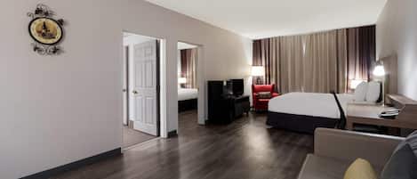 A hotel room with a bed, a desk, a TV, a red chair, and a lamp.