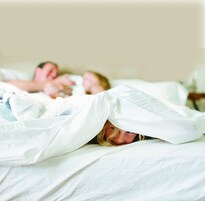 Un dormitorio con una cama cubierta con sábanas blancas y una colcha blanca.