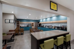 A modern kitchen with blue cabinets, a central island, and a dining area with wooden tables and chairs.