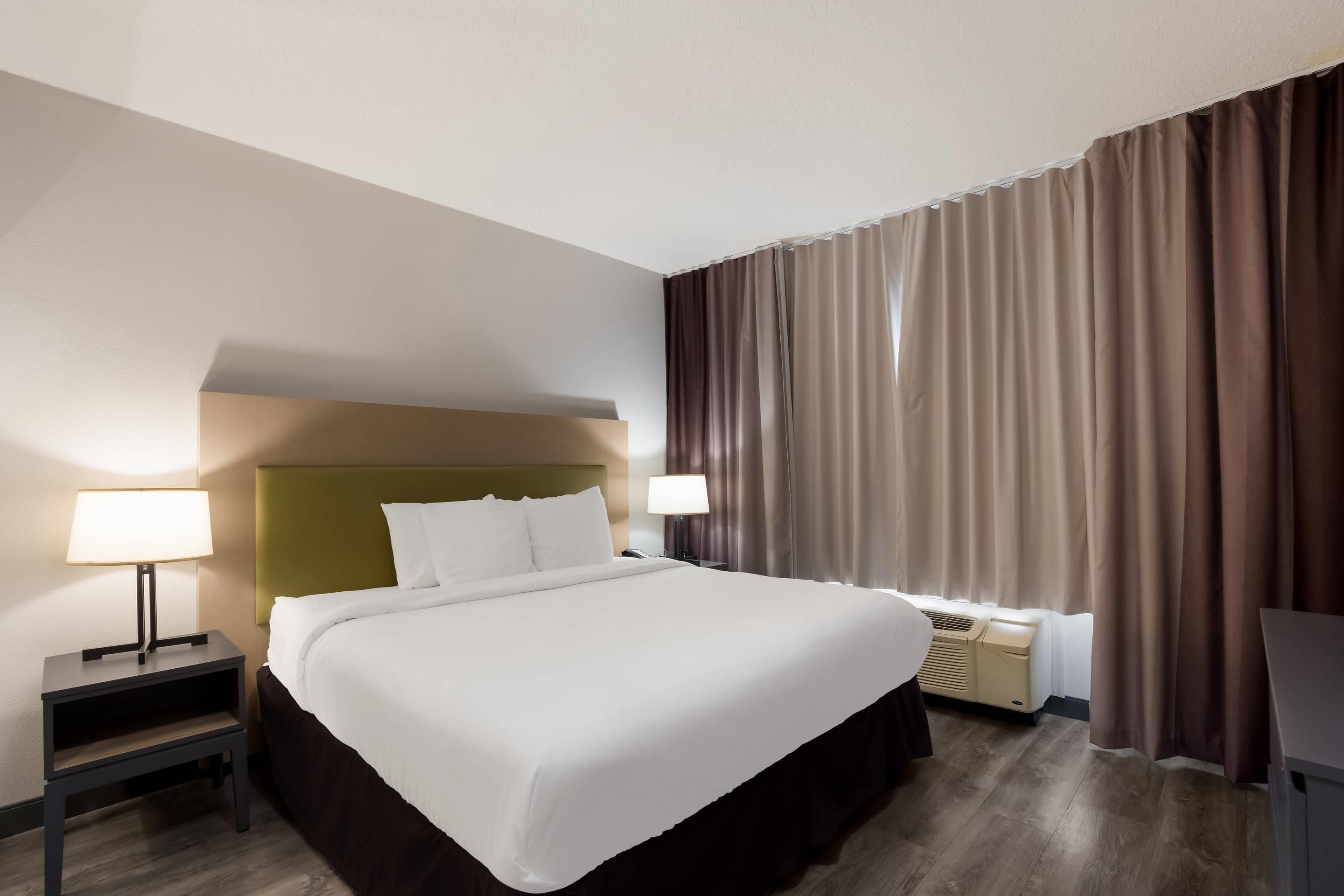 A hotel room with a bed, nightstands, lamps, a desk, and a window with curtains.