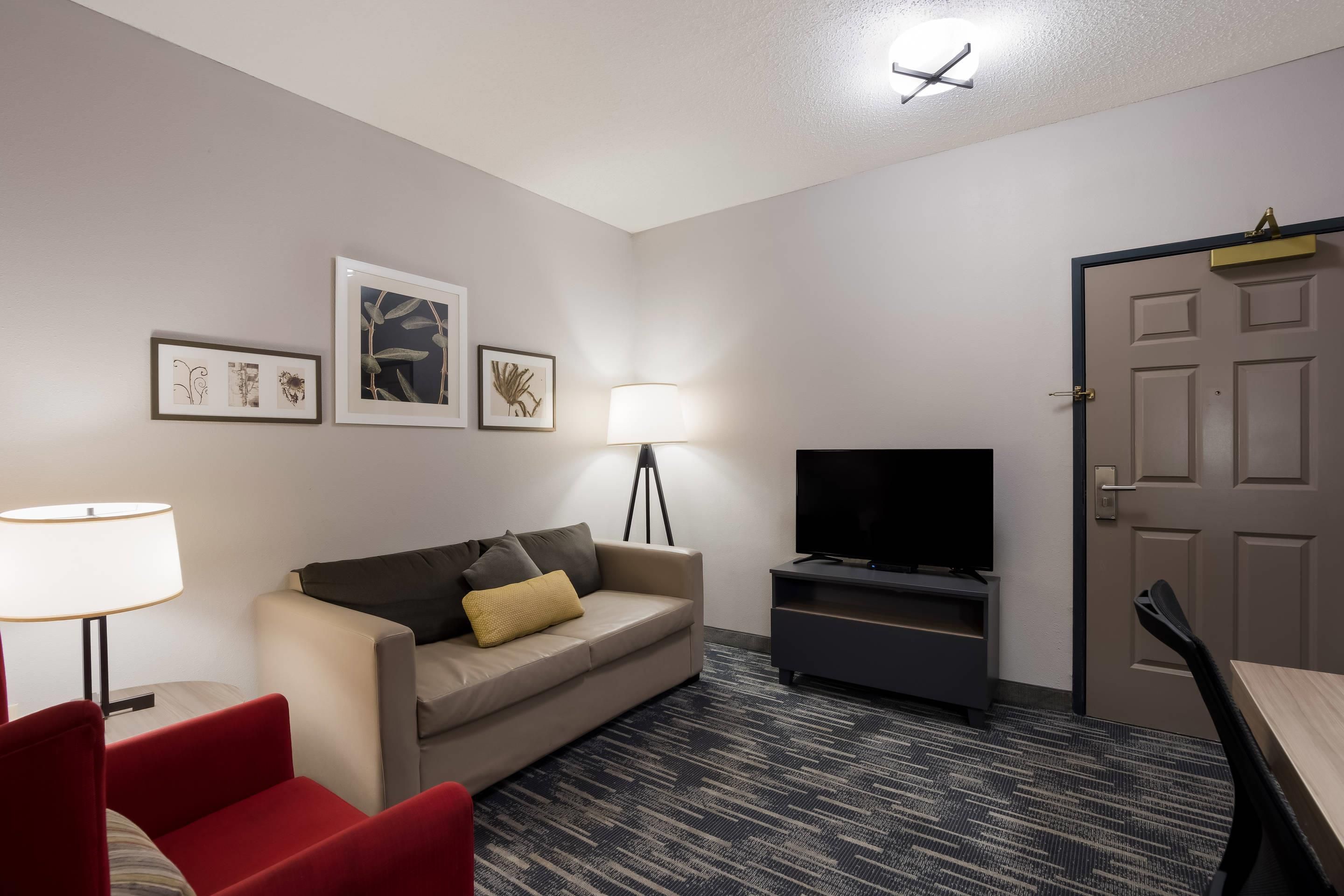 A modern living room with a sofa, a red chair, a TV, and framed artwork on the wall.