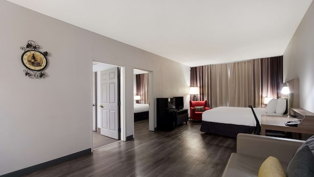 A hotel room with a large bed, a red armchair, a sofa, a desk with a lamp, a television, and a clock on the wall. - Country Inn & Suites by Radisson, Augusta at I-20, GA (Augusta)