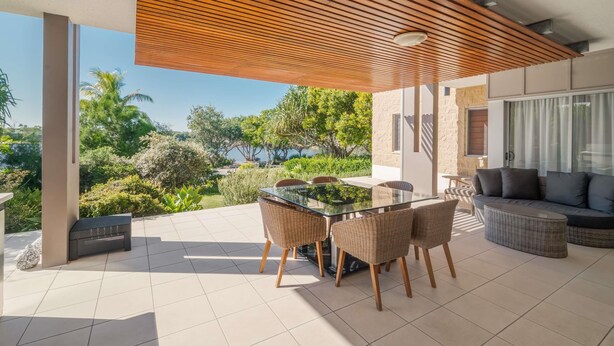 An outdoor patio with a glass-top table surrounded by wicker chairs, a sofa, and a view of a natural landscape. - The Sebel Twin Waters (Twin Waters)