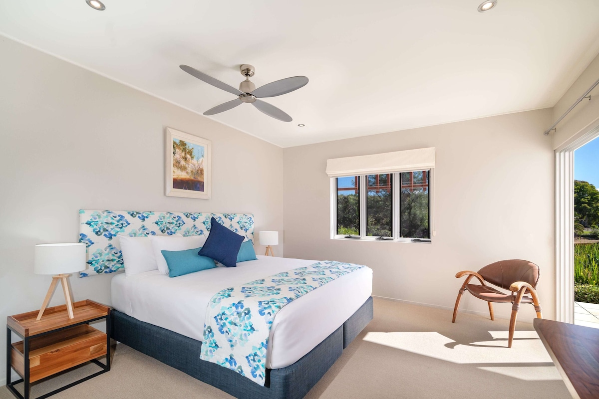 Une chambre à coucher avec un lit, un ventilateur de plafond, une fenêtre et une chaise.