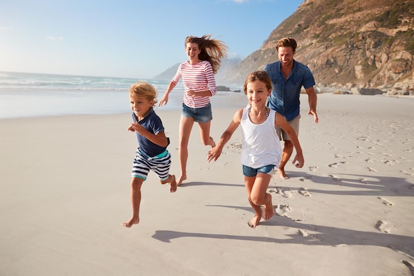 Une famille court sur une plage de sable, avec une falaise rocheuse en arrière-plan.