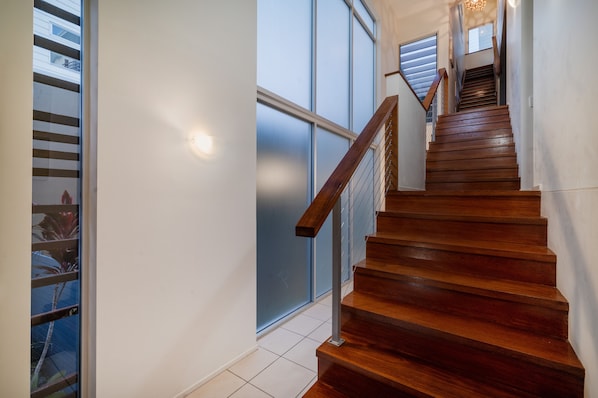 Una escalera de madera con barandilla de metal que lleva a un rellano con puerta de cristal.