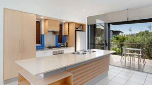 A modern kitchen with a large island, built-in cabinets, and a view to an outdoor balcony. - The Sebel Twin Waters (Twin Waters)