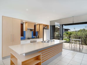 A modern kitchen with a large island, built-in cabinets, and a view to an outdoor balcony. - The Sebel Twin Waters (Twin Waters)