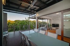 A modern living room with a glass door leading to a balcony, a flat-screen TV, and a dining area with a table and chairs. - The Sebel Twin Waters (Twin Waters)