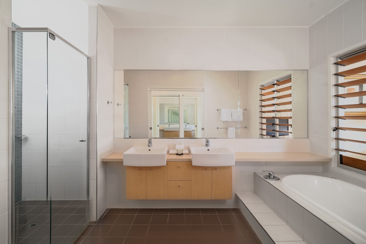Une salle de bain moderne avec deux lavabos, un grand miroir, un espace douche et une baignoire.