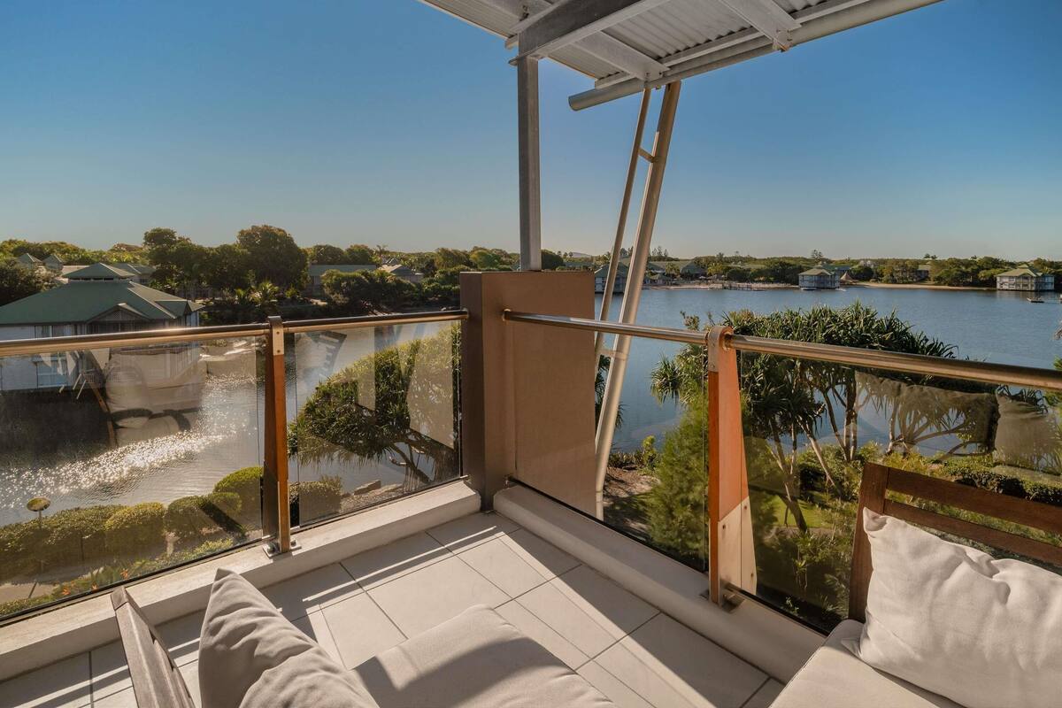 Een balkon met uitzicht op een meer, een hekwerk en een heldere lucht.
