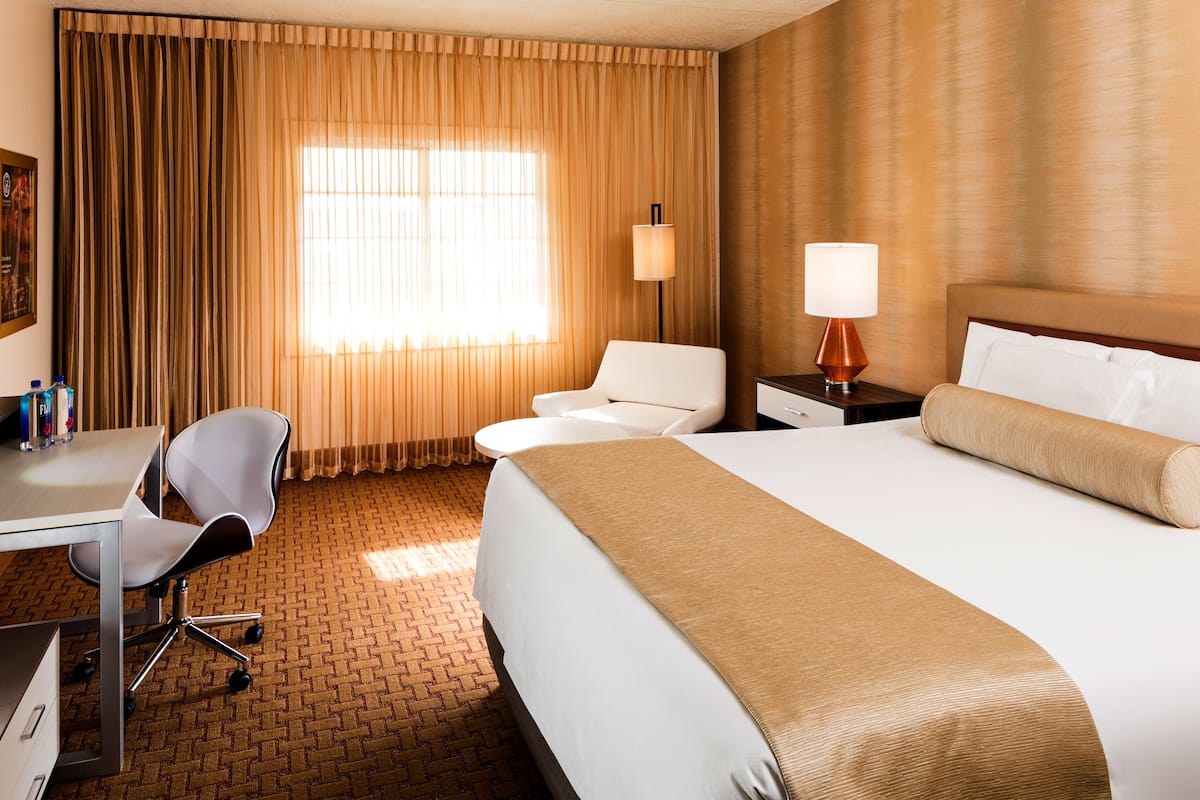 Une chambre d’hôtel avec un grand lit, un bureau avec une chaise, une lampe et une fenêtre avec des rideaux.