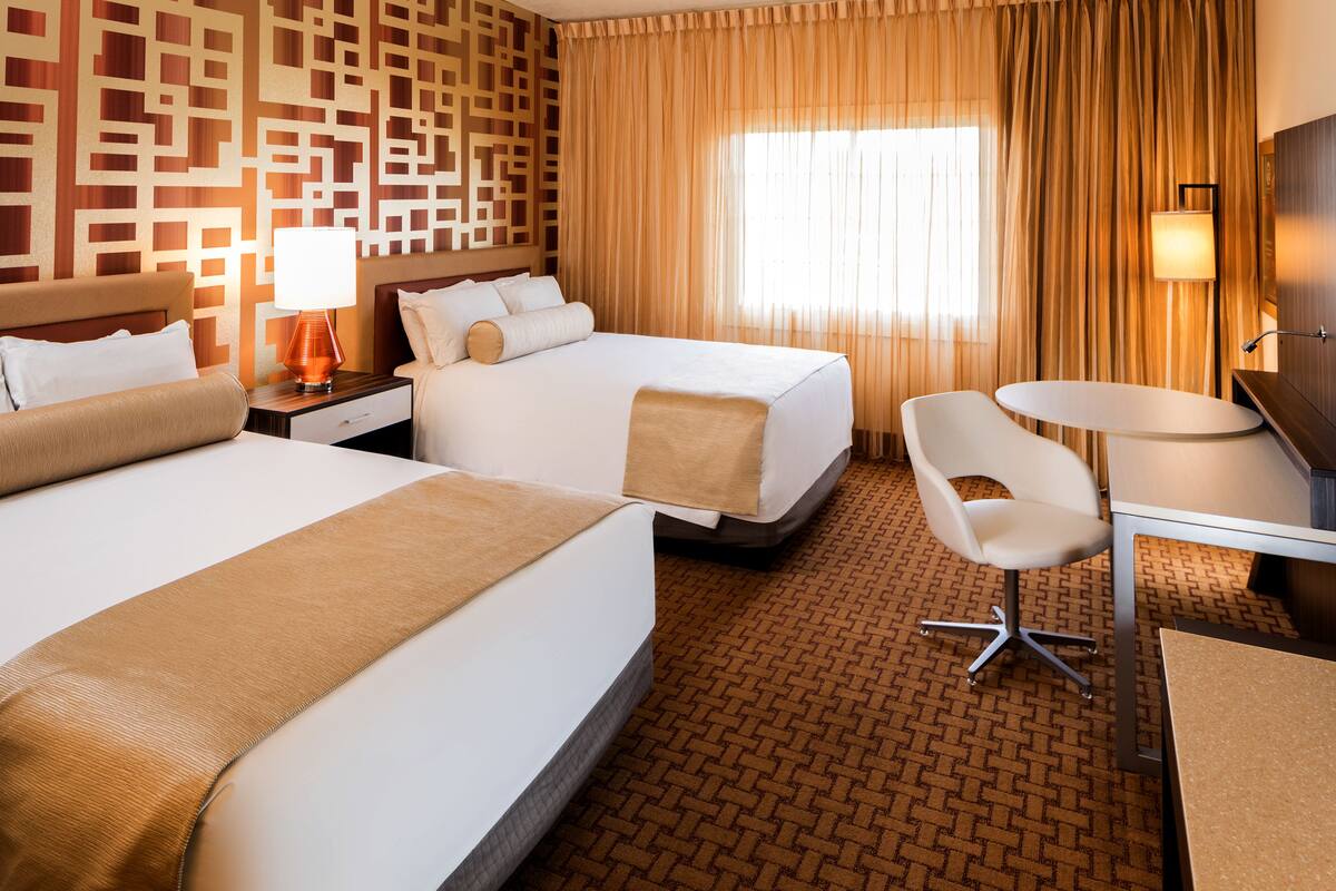 Une chambre d’hôtel avec deux lits, un bureau, une chaise, une lampe et un mur décoré d’un motif.