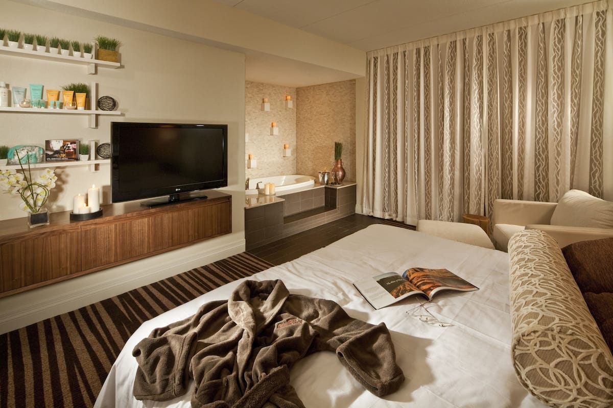 Une chambre d’hôtel moderne dotée d’un grand lit, d’une télévision, d’une salle de bain avec baignoire et d’un coin salon avec un canapé et une table basse.