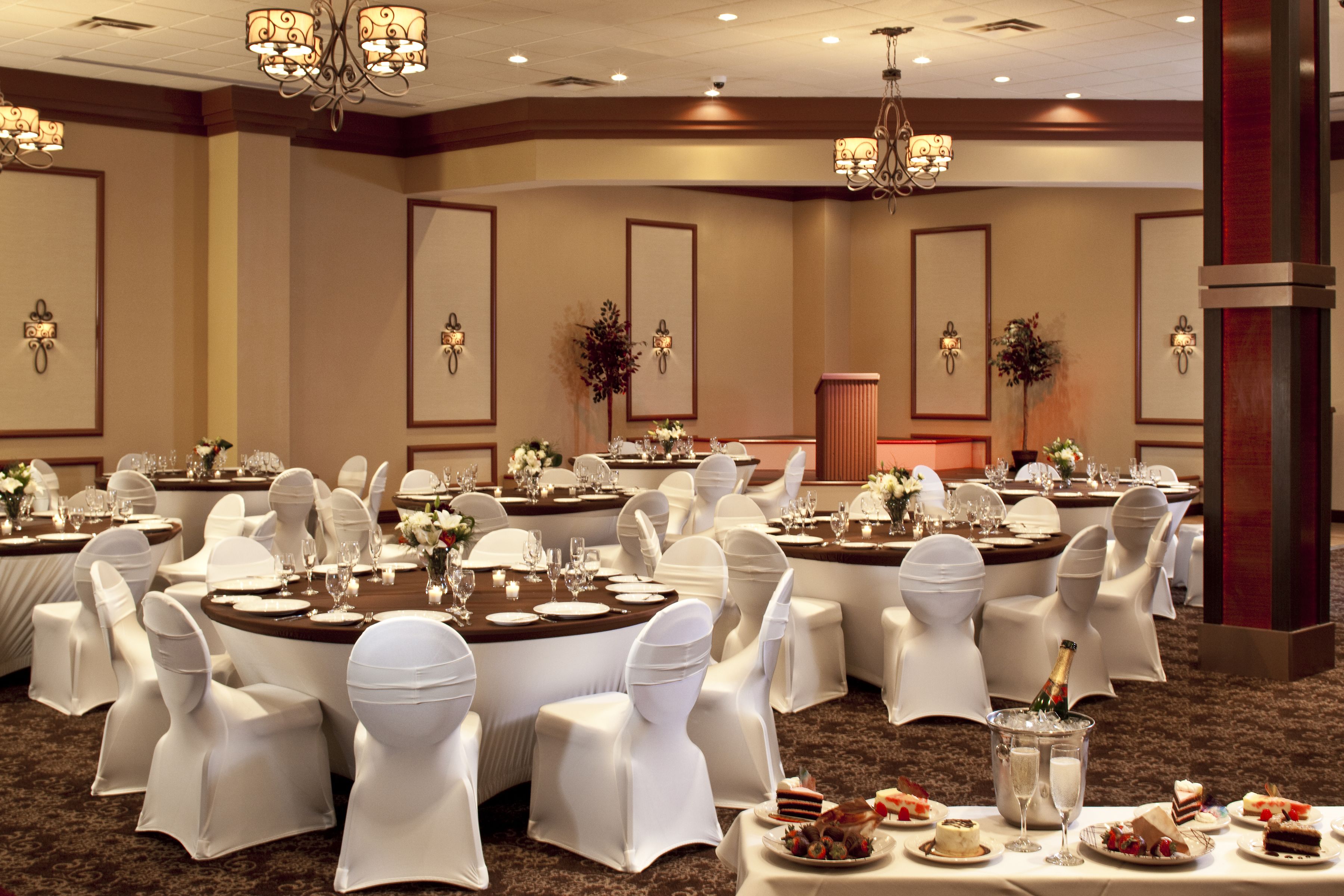 A banquet hall with round tables, white chairs, and chandeliers.