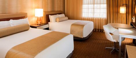A hotel room with two beds, a desk, and a chair.