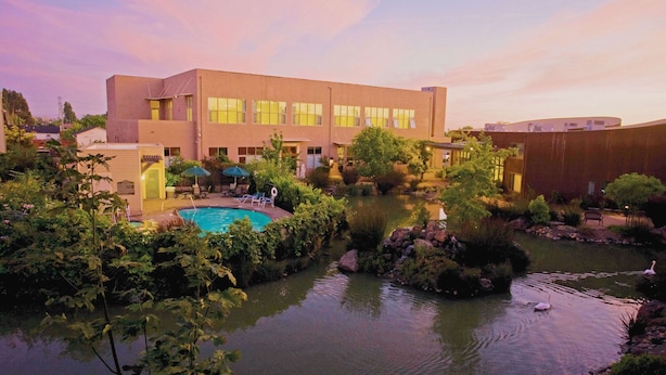 A modern building with a swimming pool surrounded by greenery and a small pond with swans. - DoubleTree by Hilton Napa Valley - American Canyon (American Canyon)