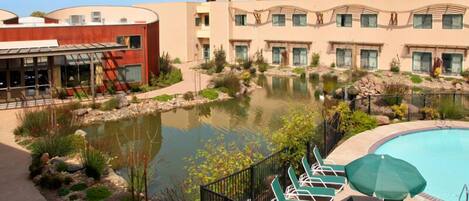 Un hotel con piscina, mobiliario exterior y un estanque.