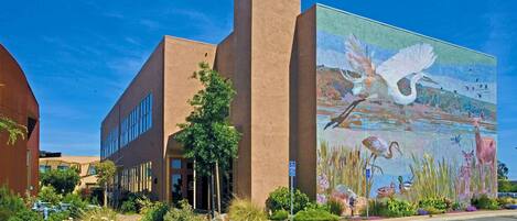 Un edificio con un mural de fauna en la fachada, un estacionamiento y un cielo azul despejado.