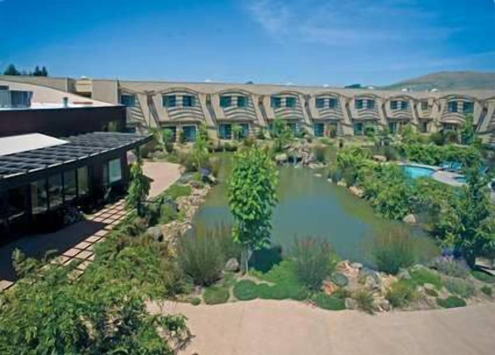 Un hotel con piscina, un giardino con uno stagno e un edificio dal design architettonico unico.