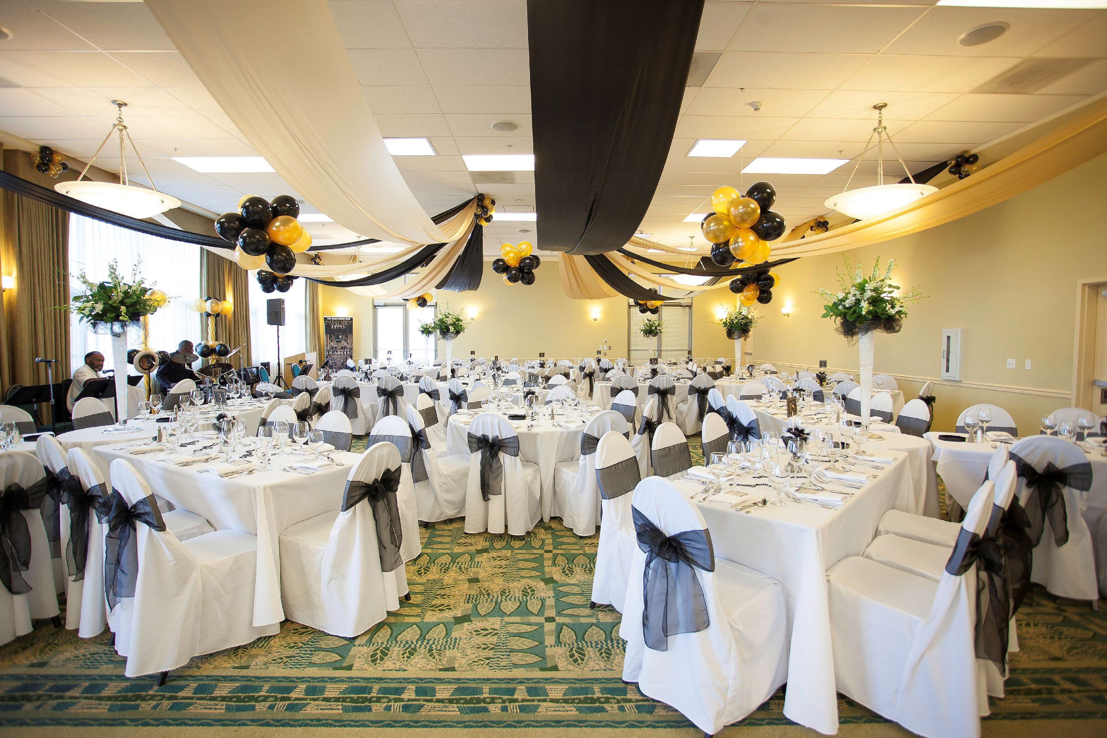 A banquet hall with round tables set for a formal event, featuring white tablecloths and chairs with black sashes.