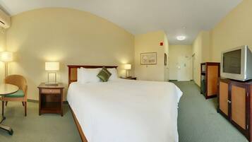 Habitación de hotel con una cama grande, mesitas de noche con lámparas, una silla, un televisor y una puerta que da a otra habitación.