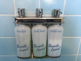 A bathroom with a soap dispenser rack holding three bottles labeled 'shampoo', 'body wash', and 'conditioner', all branded 'Beverly Laurel'.