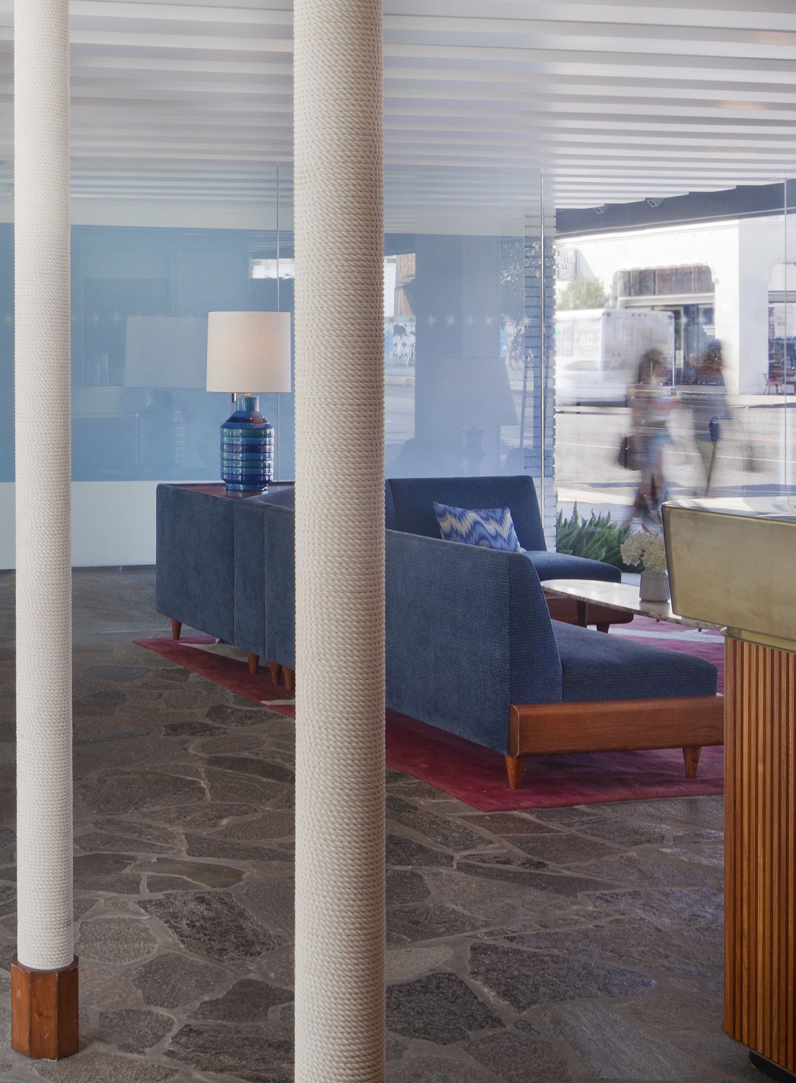 Eine moderne Lobby mit einem blauen Sofa, einer Lampe und einem Steinfußboden.