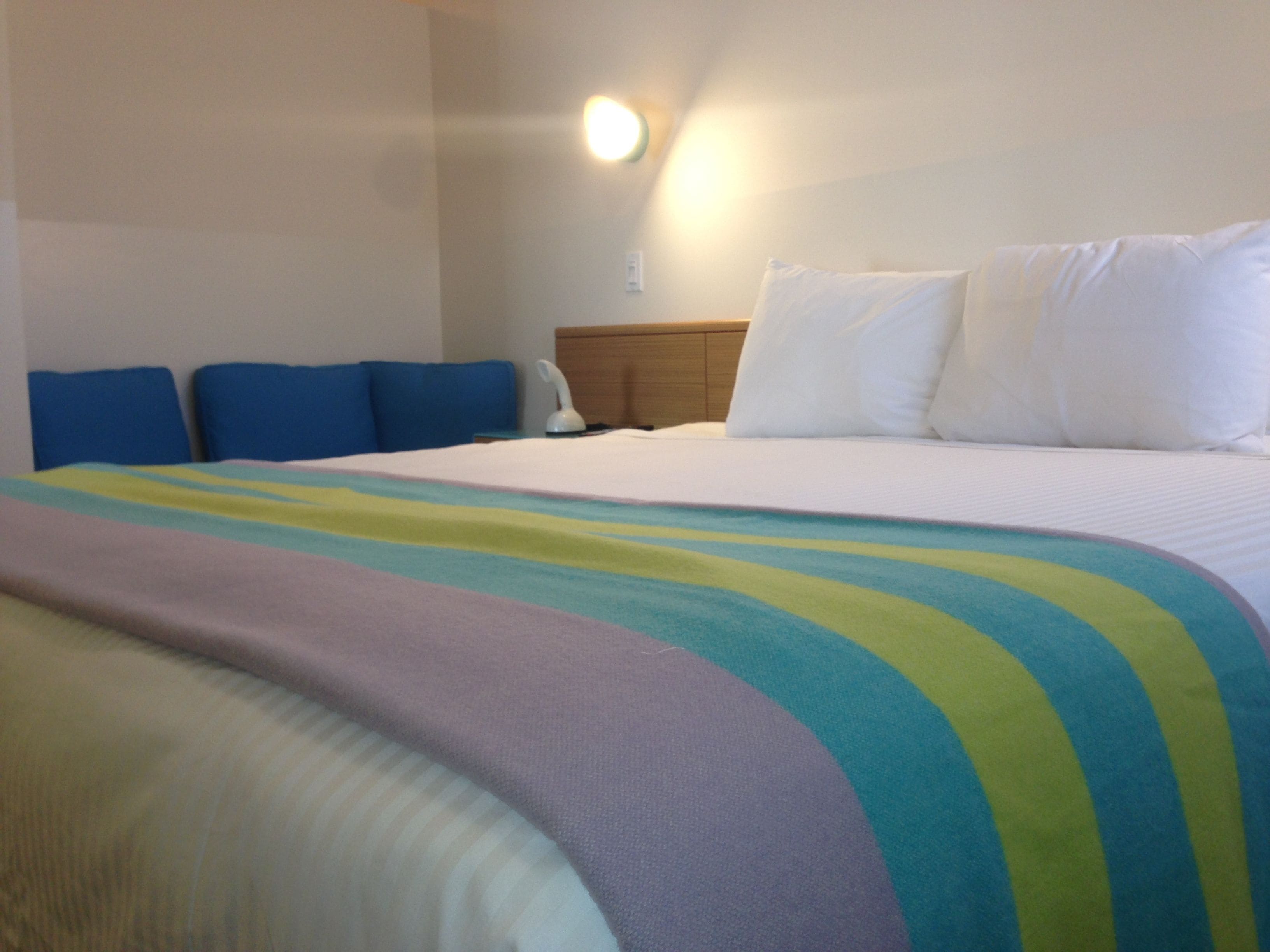Camera d'albergo con un letto, testate blu, un comodino e una lampada a parete.