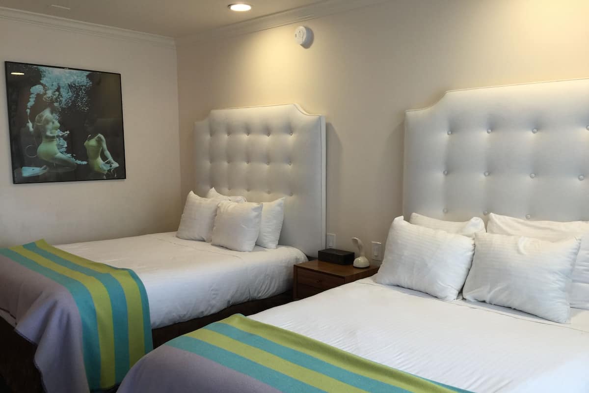 A hotel room with two beds, each with white bedding and a striped blanket. There is a painting on the wall and a nightstand with a lamp.