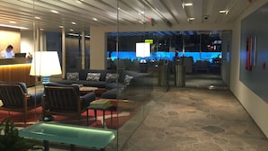 A modern lobby with a reception desk, seating area, and a glass partition leading to a bar area.