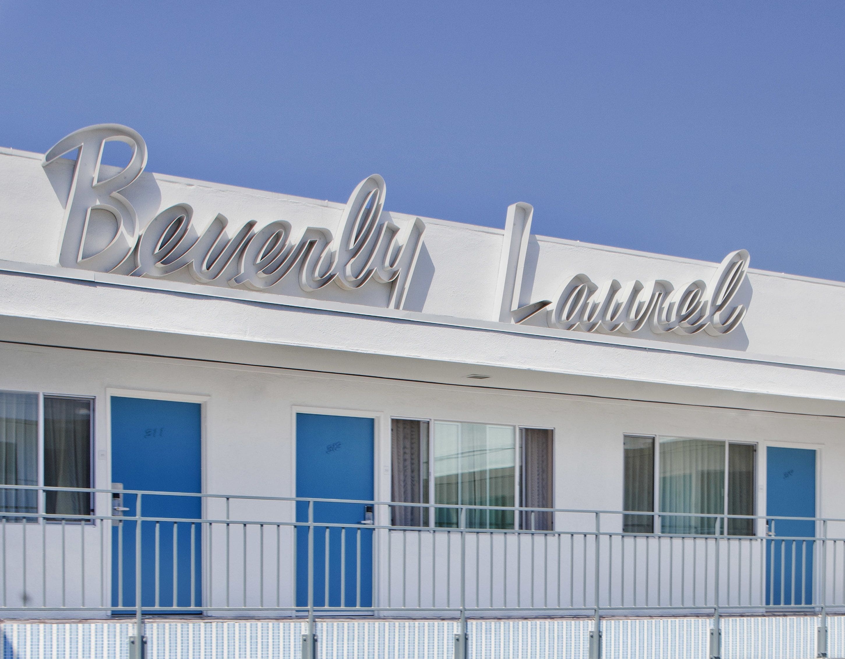 Een hotel met een bord waarop 'Beverly Laurel' staat en een rij blauwe deuren.