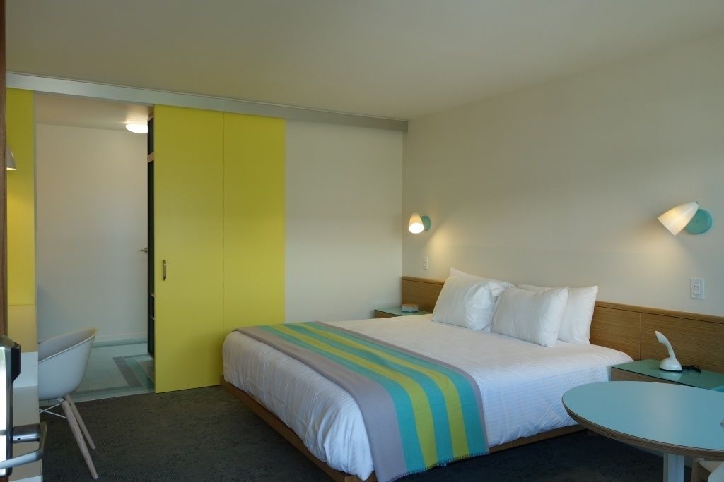 A hotel room with a bed, bedside table, lamp, and a small round table.