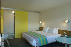 A hotel room with a bed, bedside table, lamp, and a small round table.