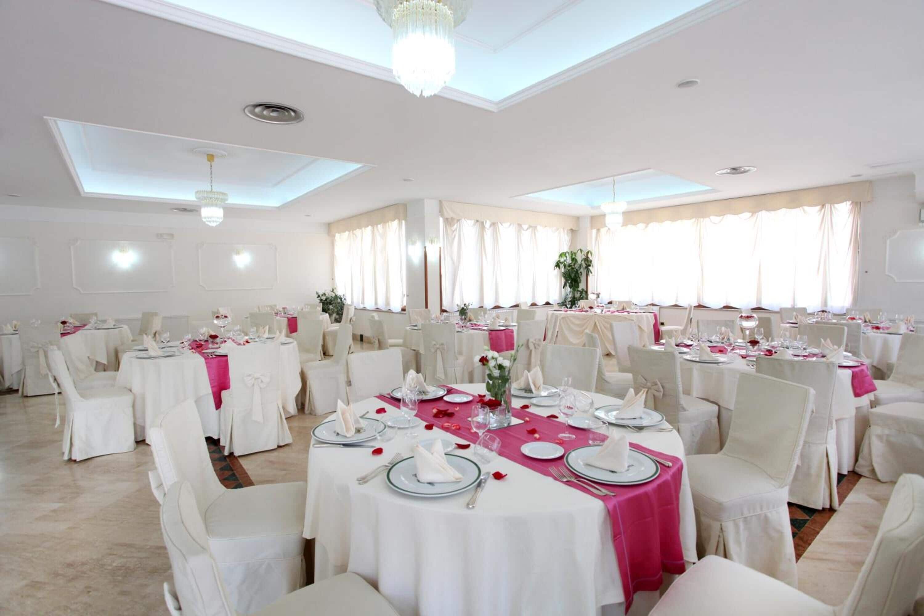 A banquet hall with round tables, white chairs, and pink tablecloths.
