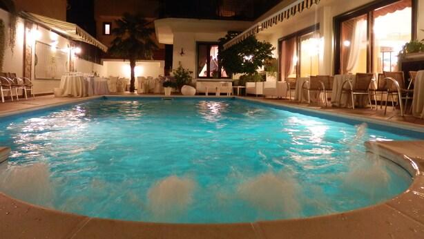 Uma área de piscina com espreguiçadeiras e mesas, cercada por um edifício com varandas e janelas amplas.