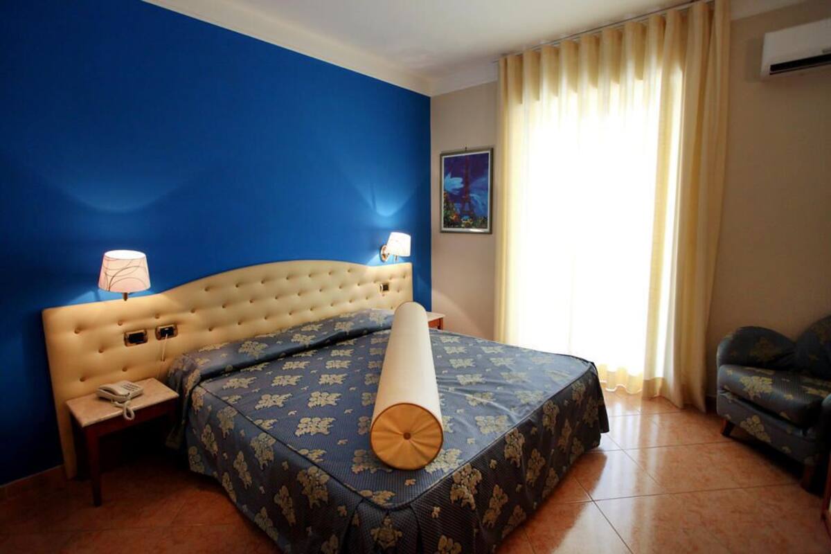 A hotel room with a large bed, a nightstand, a lamp, a sofa, and a painting on the wall.