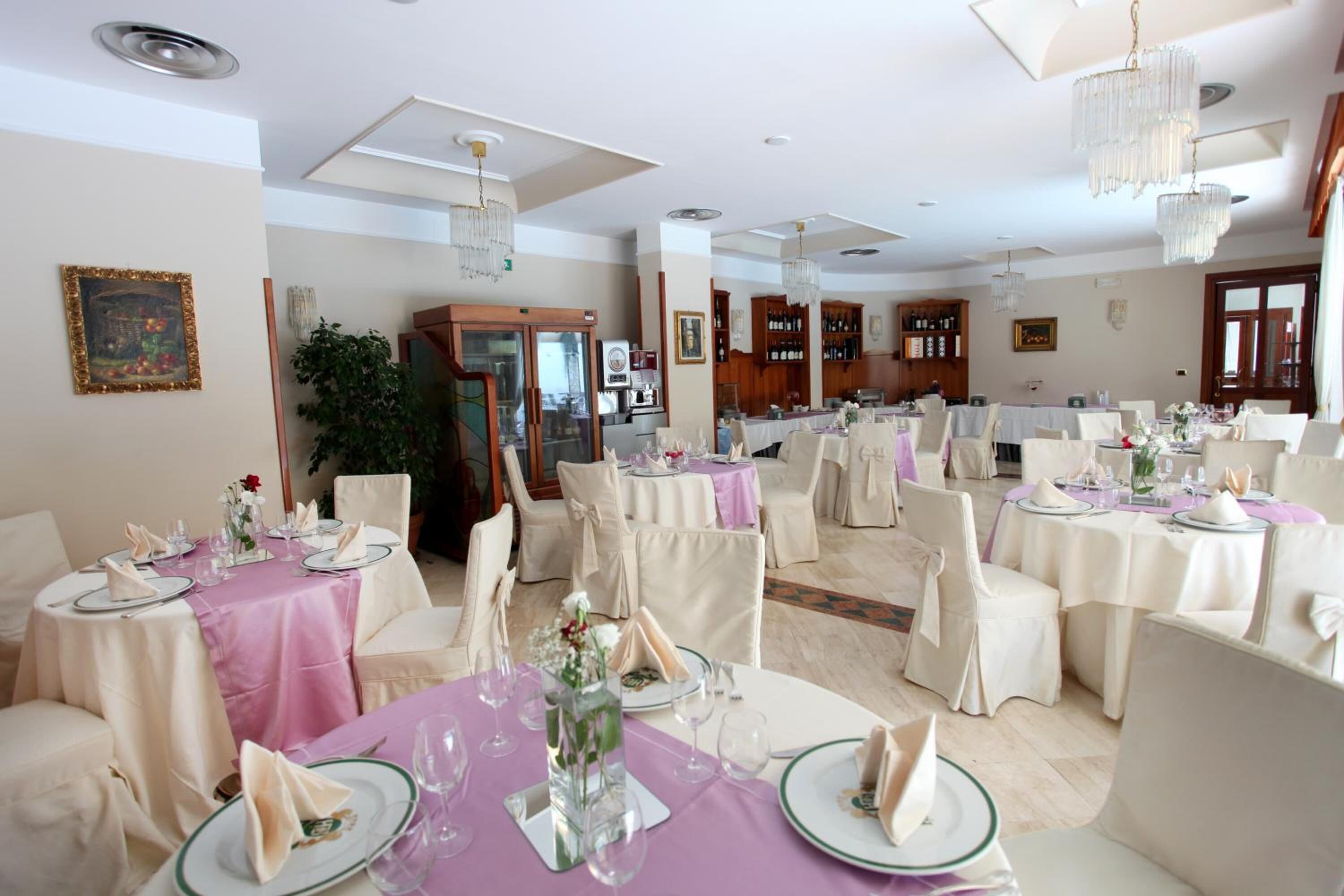 Un comedor formal con mesas redondas, sillas blancas y candelabros.