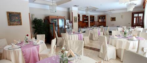 Un comedor formal con mesas redondas, sillas blancas y candelabros.