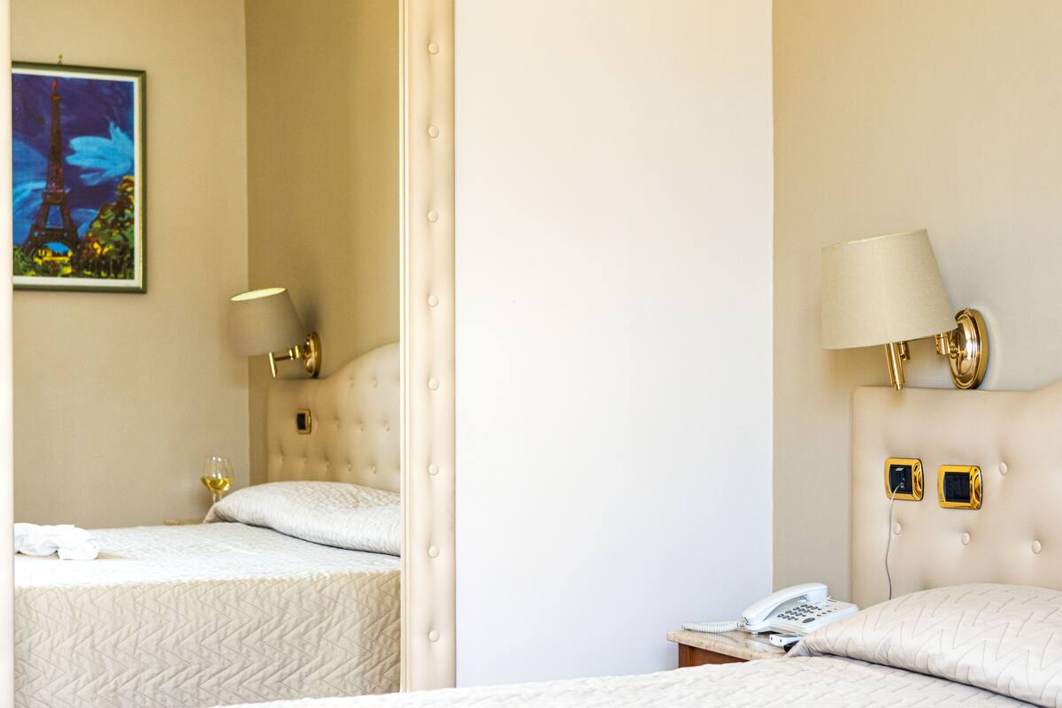A hotel room with two beds, a painting of the Eiffel Tower, a lamp, and a phone on the nightstand.