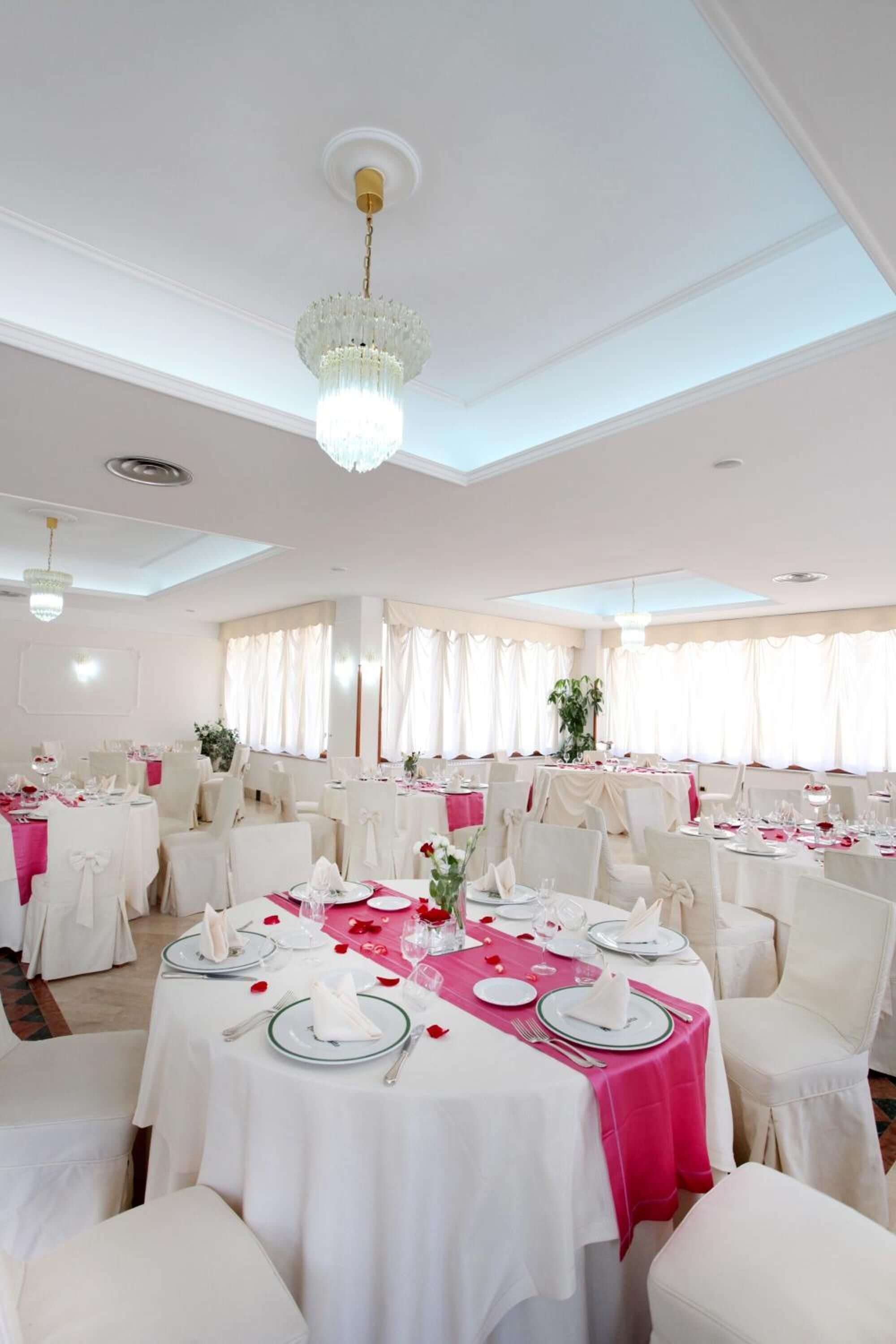 A banquet hall with round tables, white and pink tablecloths, and white chairs.
